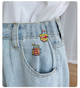 Detail of self love potion and juice enamel pins styled on a denim pocket edge