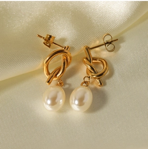 Macro shot of gold-plated knot earrings with white baroque pearls on silk fabric