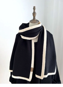 Detailed view of black knitted scarf with beige stripes on a wooden mannequin
