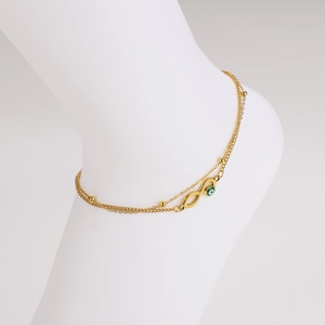 Detail of gold double-layer infinity anklet with green evil eye charm and metal beads