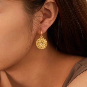 Close-up of gold-plated stainless steel starburst disc earrings on a model's ear