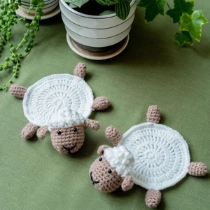 Detail of two handmade crochet sheep coasters in white and brown cotton yarn on a table
