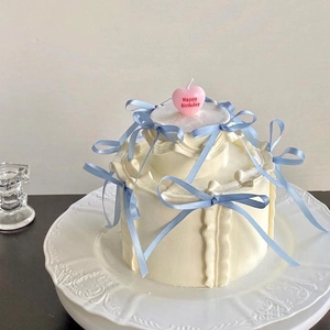 Elegant tiered cream cake with blue ribbons and pink heart Happy Birthday candle