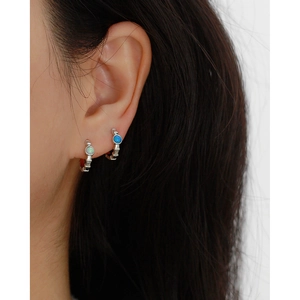 Close-up of a s925 silver hoop earring with blue opal stone worn by a female model
