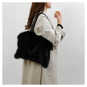 Detail of plush black faux fur shoulder bag with woven leather handle and gold hardware