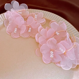 Close-up of pink tulle flower earrings with beads on gold hoops in a ceramic tray