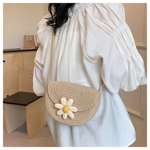 Close-up of woven shoulder bag featuring floral 3D daisy accents and saddle shape