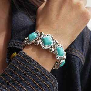 Detail of vintage geometric turquoise bracelet with silver embossed frame on denim sleeve