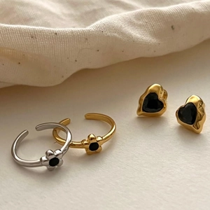 Detail of vintage heart earrings and flower open rings set on cream textured fabric