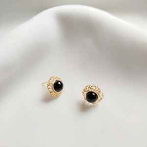 Macro detail of 925 silver black agate stud earring on white silk fabric background