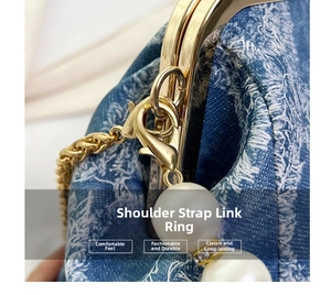 Detailed close-up of golden metal clasp with a white pearl charm on denim shoulder bag