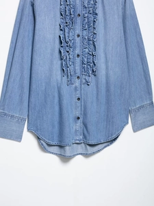 Detail of light blue denim shirt featuring ruffled frill trim and metal buttons
