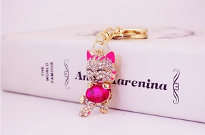 Close-up of sparkling lucky cat keychain with pink gemstones resting on a white book