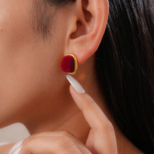 Detail of red velvet geometric earrings with gold trim worn by a model