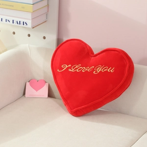 Detail of red heart plush pillow with golden I Love You embroidery on a soft beige sofa