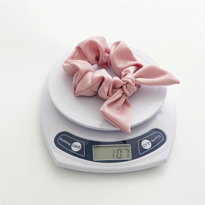 Pink fabric bow scrunchie with rabbit ear design shown on a scale weighing 10.7g