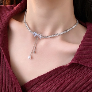 Close-up of zircon bow necklace with pearl tassel on a model with deep red background