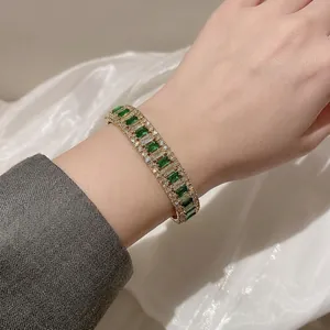 Elegant gold bangle with emerald and clear zircon stones on a white silk background