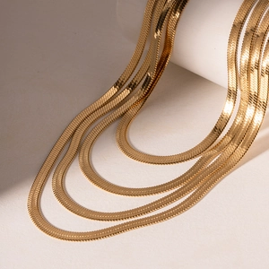 Four-layer gold snake chain necklaces with polished finish on a white display stand
