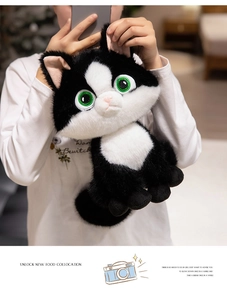 Close-up of soft black and white plush cat doll with large green eyes held by a model