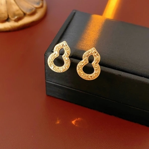 Close-up of golden gourd-shaped stud earrings with matte texture on a premium black box