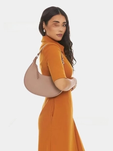 Close-up of minimalist dusty pink leather crescent bag worn by model in orange dress