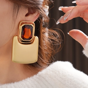 Close-up of model wearing large gold rectangle earring with amber gemstone detail