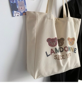 Detail view of cream canvas tote bag featuring cute bear embroidery and branded text