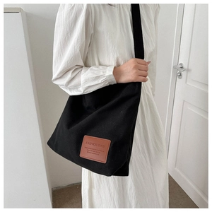 Detail shot of the black canvas tote bag with a premium brown leather logo tag