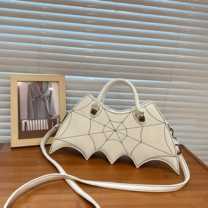 Close-up of white bat-wing shaped bag with embroidered spider web pattern on a wooden table