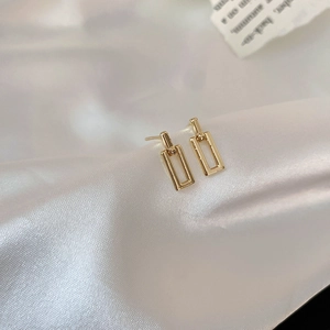 Macro detail of geometric gold rectangular double hoop earrings on white silk fabric