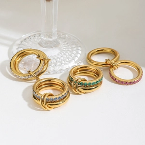 Close-up of gold-plated titanium rings with colorful zircons on a glass surface