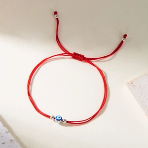 Handmade red braided Evil Eye bracelet with blue beads and silver spacers on beige background