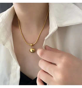 Detailed view of a minimalist golden beaded pendant necklace worn over a white shirt