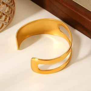 Close-up of a matte gold hollow bangle with asymmetrical open design on a tabletop