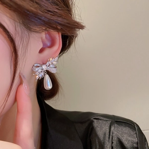 Close-up of bow knot stud earrings with marquise cubic zirconia and teardrop pearl drop