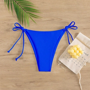 Flat lay of royal blue side-tie bikini bottoms on wood with tropical palm leaf decor