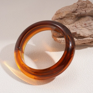 Nahaufnahme des bernsteinfarbenen Acryl-Armreifs auf Naturstein und Texturoberfläche