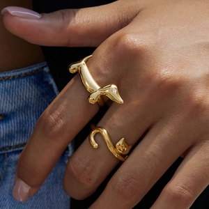 Detailed view of two gold animal rings featuring a dachshund and cat on a model hand