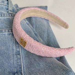 Dettaglio di un cerchietto in tweed rosa con ornamento in metallo dorato su jeans