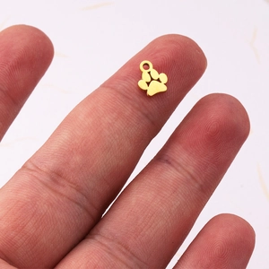 Mirror polished 18k gold plated dog paw pendant shown on fingertip for scale