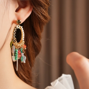 Close-up of golden leaf tassel earrings with green gemstones on female model