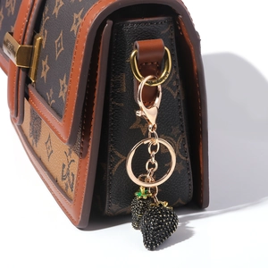 Detail of a black strawberry charm with gold metal chain on a patterned leather handbag