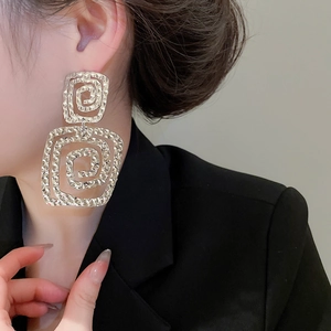 Macro detail of silver square spiral earrings with hammered texture and modern design