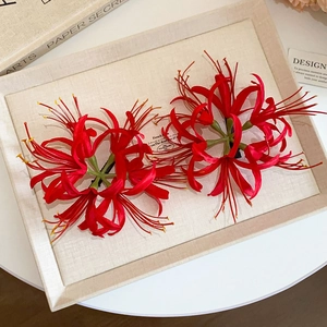 Detail view of two red lycoris flower hair clips on a textured beige tray with books