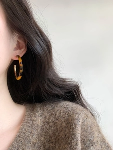 Close-up of tortoise shell resin C-shaped hoop earring worn on a model's ear