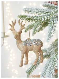 Macro detail of golden reindeer ornament with sequins hanging on a snowy pine branch