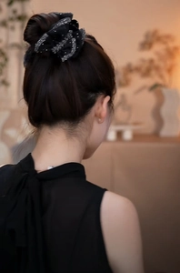 Détail d'un chouchou élégant en organza noir à paillettes argentées sur une queue de cheval