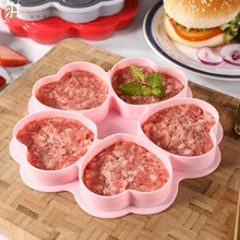 Pink heart-shaped silicone baking mold filled with raw burger patties on a wooden board