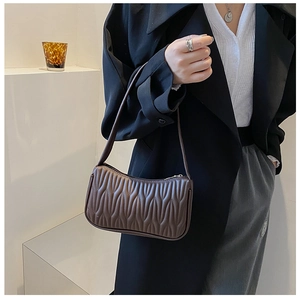 Detailed close-up of a dark brown quilted baguette bag with pleated leather texture